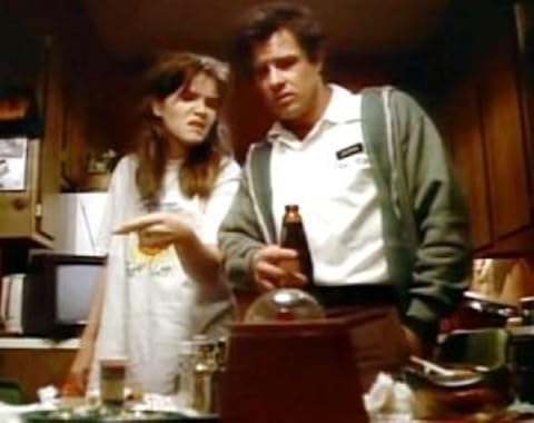 A somewhat disheveled looking man and woman are looking at a strange device on their kitchen table, perhaps arguing over it.