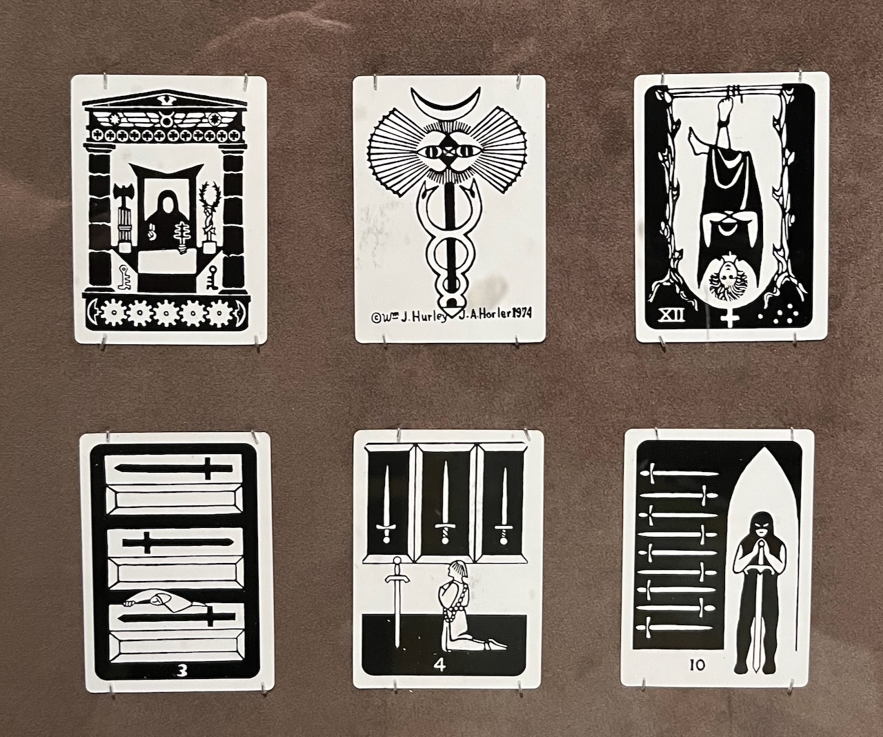 Six small, black-and-white tarot cards mounted in a museum display.