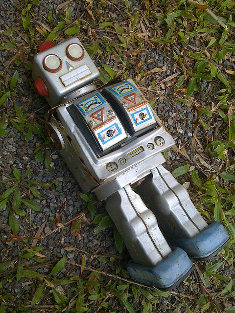 Photograph of a broken toy robot, lying in the grass.