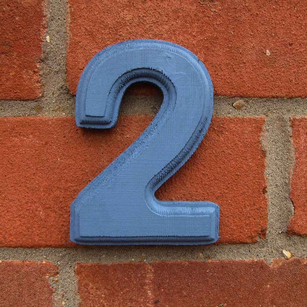 A wooden number '2' mounted on a brick wall.