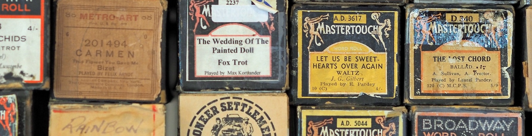 A stack of ancient piano rolls in boxes, with labels like 'The Wedding of the Painted Doll: Fox Trot' and 'Let us be Sweethearts Over Again: Waltz'.