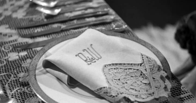 A still from the film 'Rebecca', depicting a fancy folded dinner napkin monogrammed with 'R de W'.
